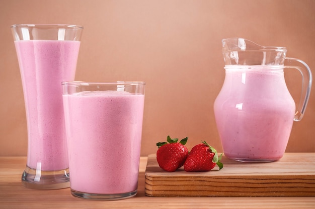 Kruik en glazen met voedzame aardbeienmilkshake op een houten tafel