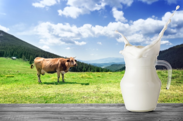 Foto kruik melk met plons met bruine koe in bergen