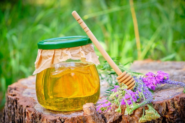Kruikhoning en lepel voor honing in bos op stomp met weidebloemen