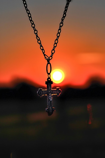 Foto kruishanger hangend aan een ketting afgetekend tegen een prachtige zonsondergang