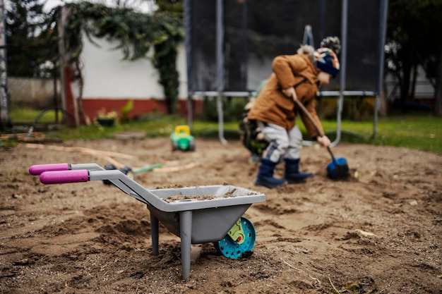 Kruiwagen speelgoed vol zand met broers die spelen met zand op een wazige achtergrond