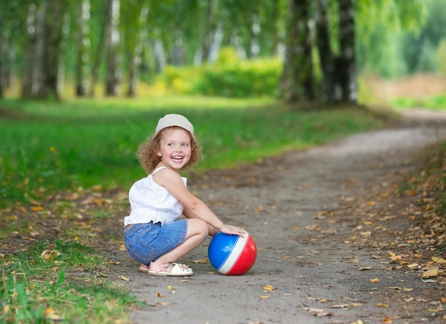 krullend blond meisje speelt met een rubberen bal in een zomerpark