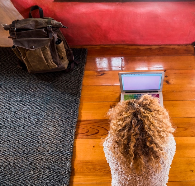 Krullend blonde vrouw die bij de laptop op de vloer in hotel of huiskamer werkt van boven gezien