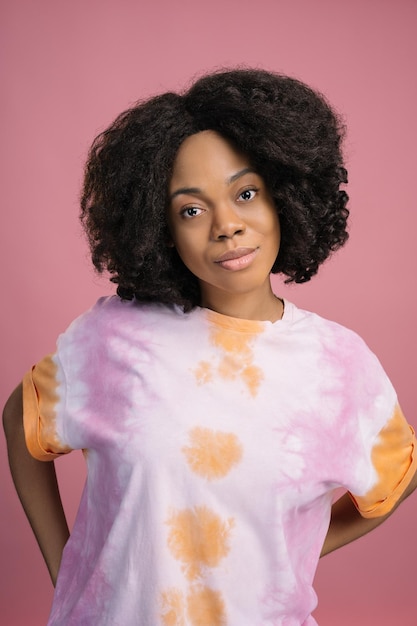 Foto krullend haired afrikaanse mannequin dragen stijlvolle tie dye t-shirt geïsoleerd op roze achtergrond