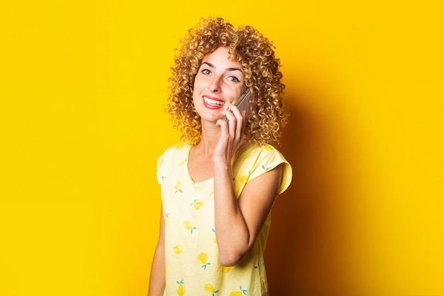 Krullend jonge vrouw die lacht praten aan de telefoon op een geel oppervlak