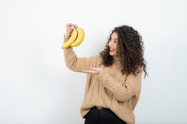 Krullend jonge vrouw met bananen over wit.
