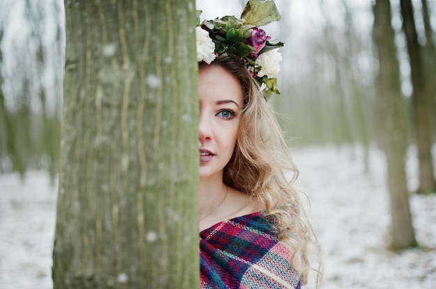 Krullend schattig blondemeisje met kroon in geruite plaid bij sneeuwbos in de winterdag.