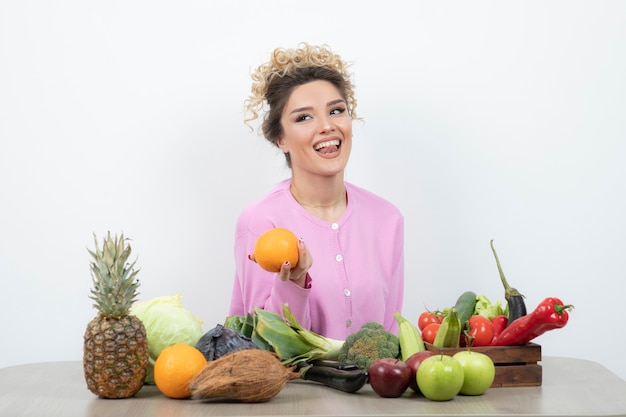 Krullend vrouw zittend aan tafel met sappige sinaasappel.