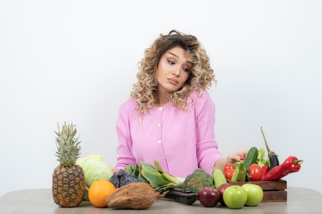 Krullend vrouw zittend aan tafel met veel verschillende verse groenten.