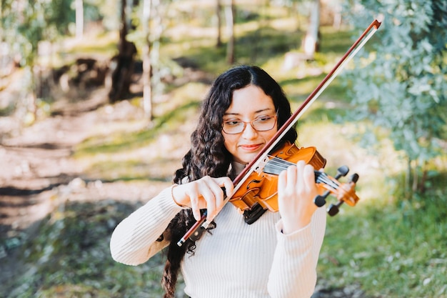 Krullende brunette vrouw met een bril die viool speelt in het bos Selectieve aandacht