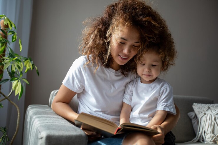 Krullende moeder en dochter in witte T-shirts die een boek lezen