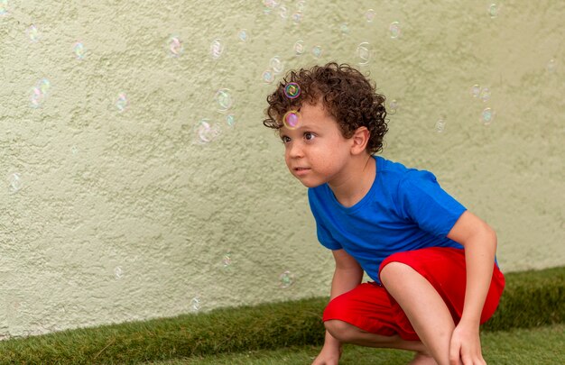 Krullendharige jongen met sproeten spelen in de achtertuin met zeepbellen.