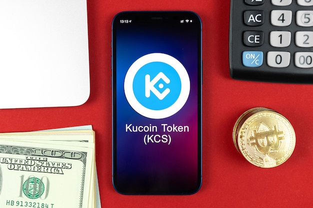 KucoinKCSトークンシンボル。暗号通貨、デジタルおよび仮想通貨で取引し、携帯電話の概念で銀行業務を行います。ビジネスワークスペース、ノートパソコンの上面写真付きテーブル