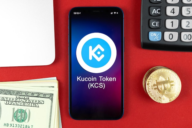 Kucoin KCS token symbool. Handel met cryptocurrency, digitaal en virtueel geld, bankieren met concept voor mobiele telefoons. Zakelijke werkruimte, tafel met laptop bovenaanzicht foto