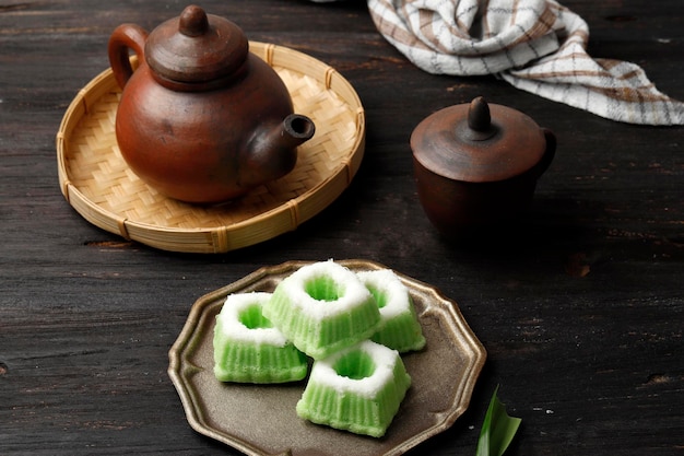 Kue Putu Ayu、蒸し小麦粉とすりおろしたココナッツから作られたインドネシアの伝統的なジャジャンパサール。木製の背景にお茶を添えて