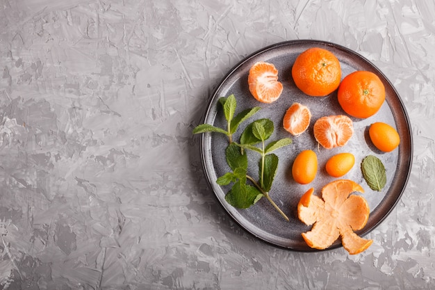 Kumquats en een tak van munt op keramische plaat op grijs