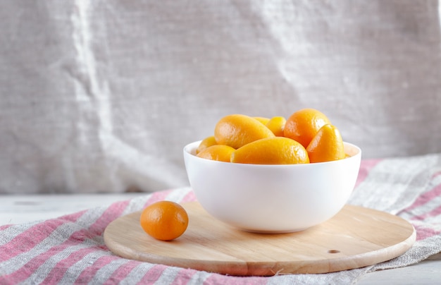 Kumquat in un piatto bianco su una tavola di cucina in legno