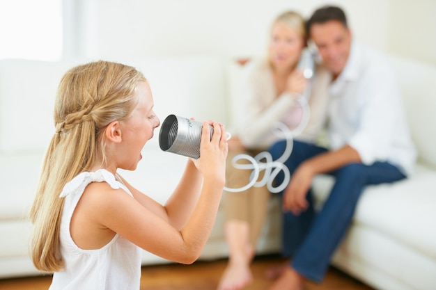 Kun je me horen Een klein meisje dat luid schreeuwt in een blikje dat is verbonden met haar ouders op de achtergrond