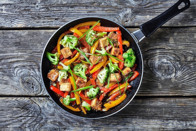 Kung pao tofu with mixed peppers, broccoli and scallions in a skillet on a rustic wooden table, chinese cuisine, landscape view from above