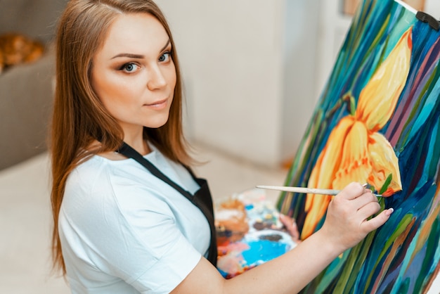 Kunst, het werk van de kunstenaar. De jonge mooie meisjeskunstenaar schildert een beeld. Workshop van de kunstenaar. Het proces van creativiteit. Tekenen en schilderen. Inventaris van de kunstenaar. Detailopname.