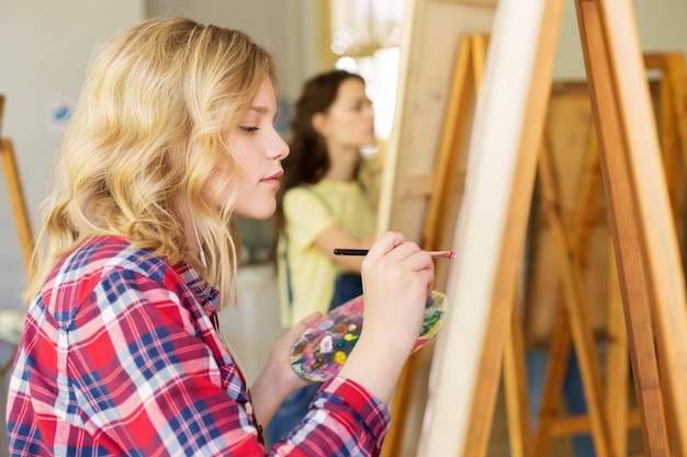Foto kunst school creativiteit en mensen concept tiener meisje met easel palet en penseel schilderen in de studio