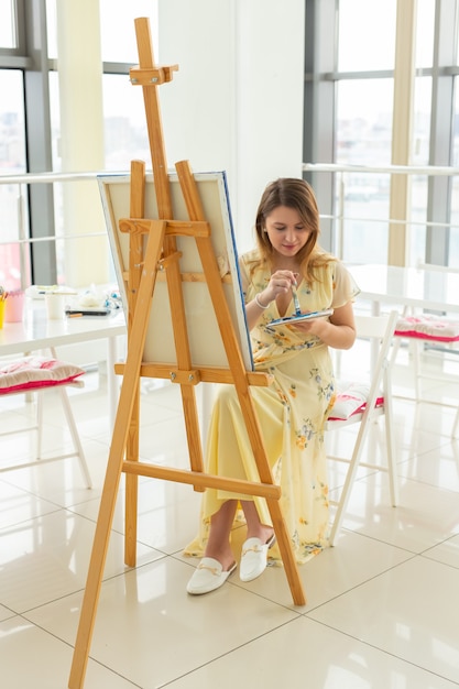 Kunstacademie, creativiteit en vrije tijdsconcept - studentenmeisje of jonge vrouwenkunstenaar met schildersezel, palet en verfborstel die beeld schilderen bij studio