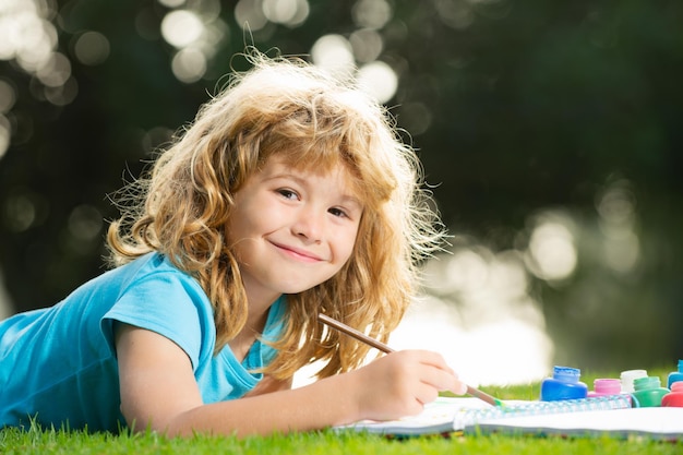 Kunstenaar kinderen kind jongen tekent in park liggend in het gras met plezier op de natuur achtergrond