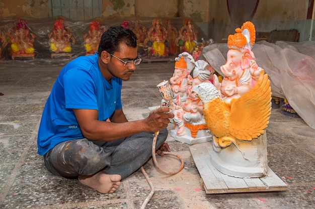 Kunstenaar maakt een standbeeld en geeft de laatste hand aan een idool van de hindoegod Lord Ganesha in een kunstenaarsatelier voor het Ganesha-festival.