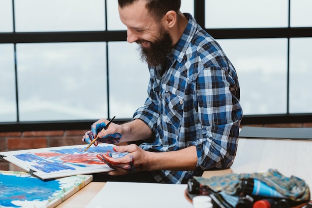 Kunstenaar verrukking Glimlachende bebaarde man met bordpaneel Schilderen inspiratie opdoen ideeën genereren vaardigheden beheersen Hobby