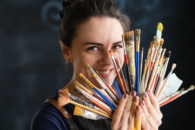 Kunstenaars en kunstbenodigdheden. Glimlachende jonge vrouw met penselenassortiment. Gereedschap ventilator opstelling.