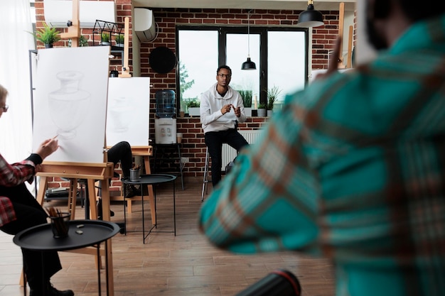 Kunstenaarsstudenten die artistieke kunstwerken op canvas maken met grafisch potlood tijdens kunstcursus in creatieve studio. Multi-etnisch team tekening vaasmodel op canvas werken bij schetstechniek.