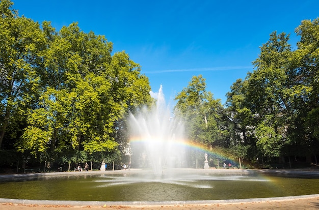 Kunstmatige fontein met weerspiegelde bellenwaterregenboog in natuurpark onder duidelijke blauwe hemel