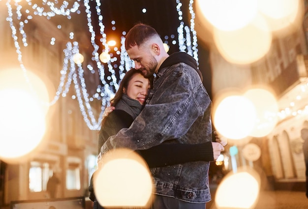 Kunstmatige verlichting door slingers Gelukkig multiraciaal paar samen buiten in de stad die Nieuwjaar viert