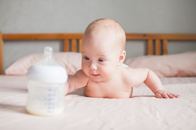 Kunstmatige voeding. De baby ligt op het buikje op haar buikje en kijkt met de aangepaste melkformule naar de fles voor hem