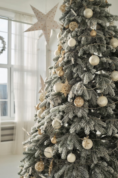 Kunstmatige weelderige gegoten besneeuwde kerstboomspar versierd met witgouden ballen, kaarsenlichten, garland close-up in wit interieur