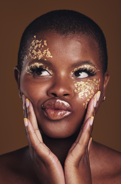 Kunstplezier en zwarte vrouw in gouden make-up op bruine achtergrond glitterverf of cosmetica Glans gloed en dom gezicht van Afrikaans model in studio voor schoonheidsmode en esthetische vrijheid in luxe huid