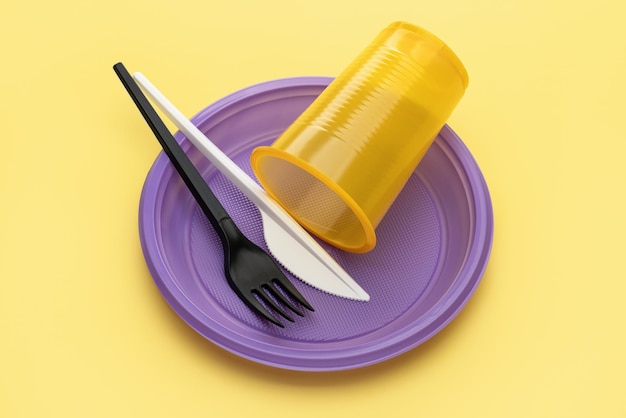 Kunststof gebruiksvoorwerpen. Gele plaat, paars glas, mes, vork op gele achtergrond, studio opname.