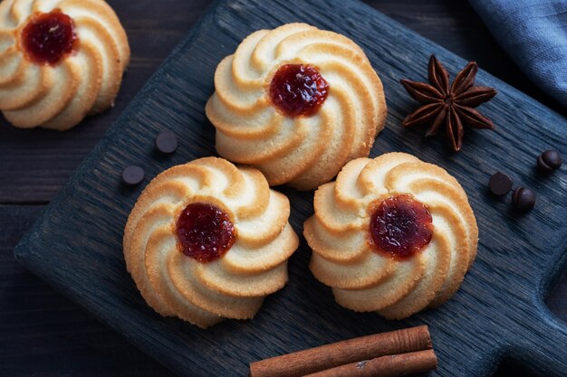 Kurabye shortbread cookies with berry jam in a black plate Delicious dessert dark wooden background