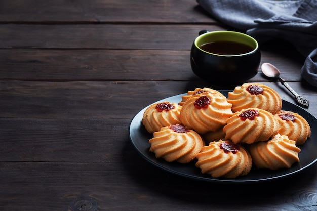 Kurabye zandkoekkoekjes met bessenjam in een zwarte plaat. Heerlijk dessert, donkere houten achtergrond met kopieerruimte.