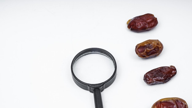 Photo kurma or dates fruits isolated with magnifiying glass on white background