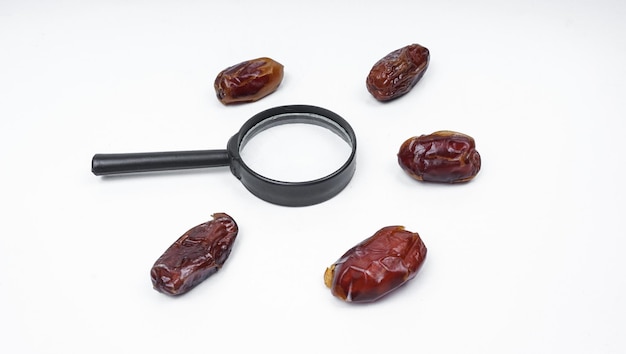 Photo kurma or dates fruits isolated with magnifiying glass on white background