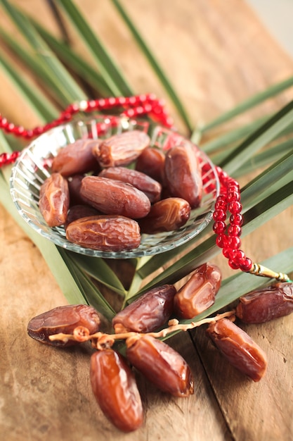 Photo kurma or dried dates, rosary on wooden background.