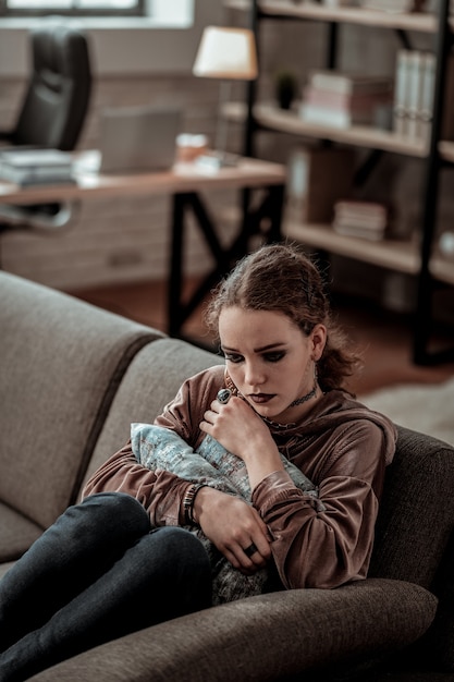 Kussen vasthouden. Donkerharige tiener met donkere make-up die een kussen vasthoudt, voelt zich extreem eenzaam en stressvol