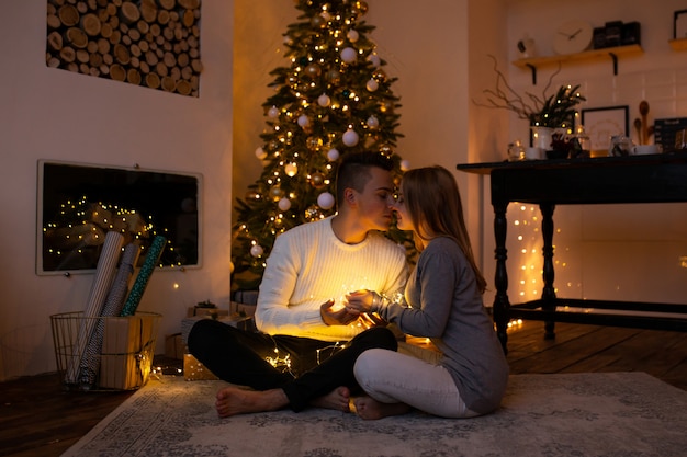 Kussend paar bij Kerstmishuis met magische lichte slinger in handen