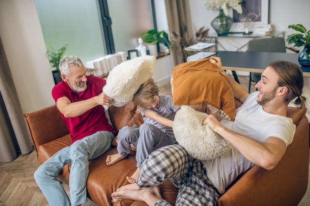 Kussengevecht. Schattige blonde jongen en twee mannen kussen vechten en vreugde voelen