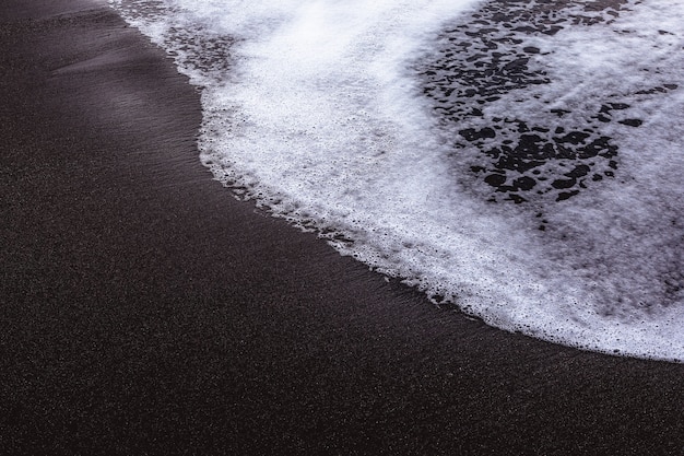 Kust met zwart zand en wit schuim