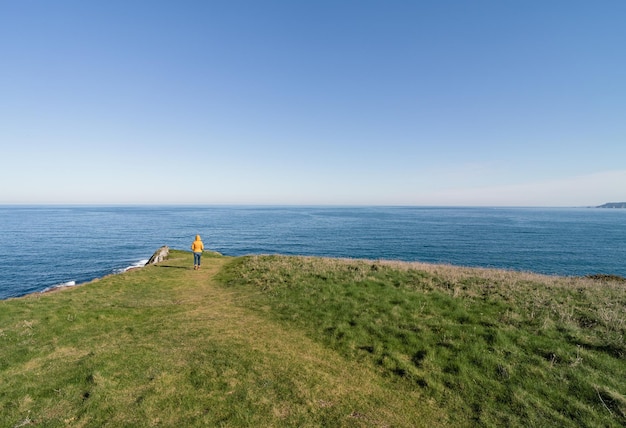 Kustlandschap en meisje in gele jas met capuchon kijken naar zee en wandelen Kopieer ruimte Horizontale foto andscape en meisje in gele jas met capuchon kijken naar zee en wandelen Kopieer de ruimte