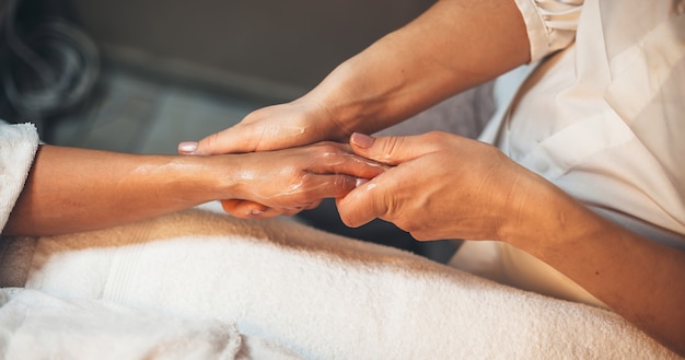 Foto kuuroordmedewerker die de hand van de klant met speciale lotion masseert tijdens een handmassagesessie in de kuuroordsalon