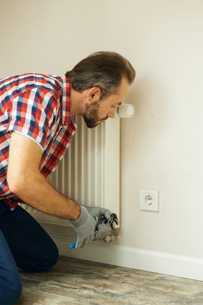 Kwaliteitshulpklusjesman die een waterpomptang gebruikt tijdens het repareren van de radiatorbatterij in de kamerverwarming