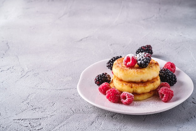 Kwark pannenkoeken en poedersuiker wrongel beignets dessert met framboos en braambessen in plaat op steen concrete achtergrond hoek weergave kopie ruimte